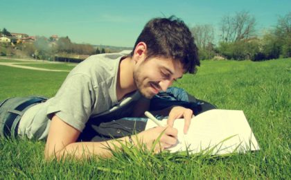 man laying on grass writing in notebook